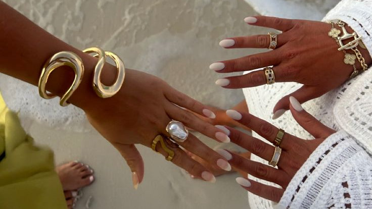 Two people's hands with jewelry on a beach
